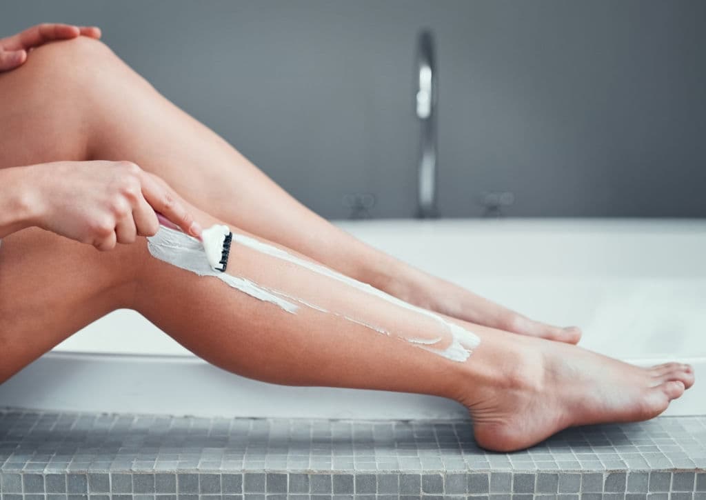woman shaving her legs in the bathroom